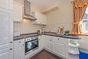 A kitchen with white cabinets, a stainless steel range hood, a built-in oven, a countertop with a coffee maker, and a window with curtains. - "Ferien am Haff" Vacation Home with Sauna, Fireplace, and Terrace - Detached (Zirchow)