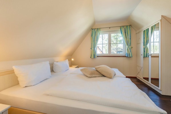 A bedroom with a bed, pillows, a bedside table, a lamp, and a window with curtains.