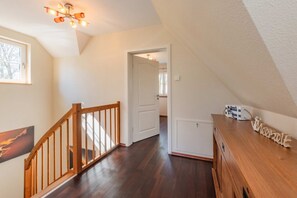Un hall d’entrée spacieux, doté d’un plancher en bois, d’une rambarde en bois, d’un luminaire au plafond et d’une porte donnant sur une autre pièce.