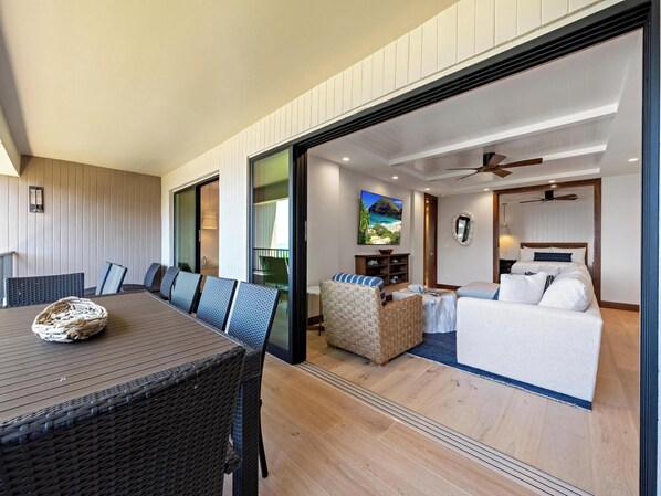 A modern living area with a dining table, wicker chairs, a sofa, and a bed.