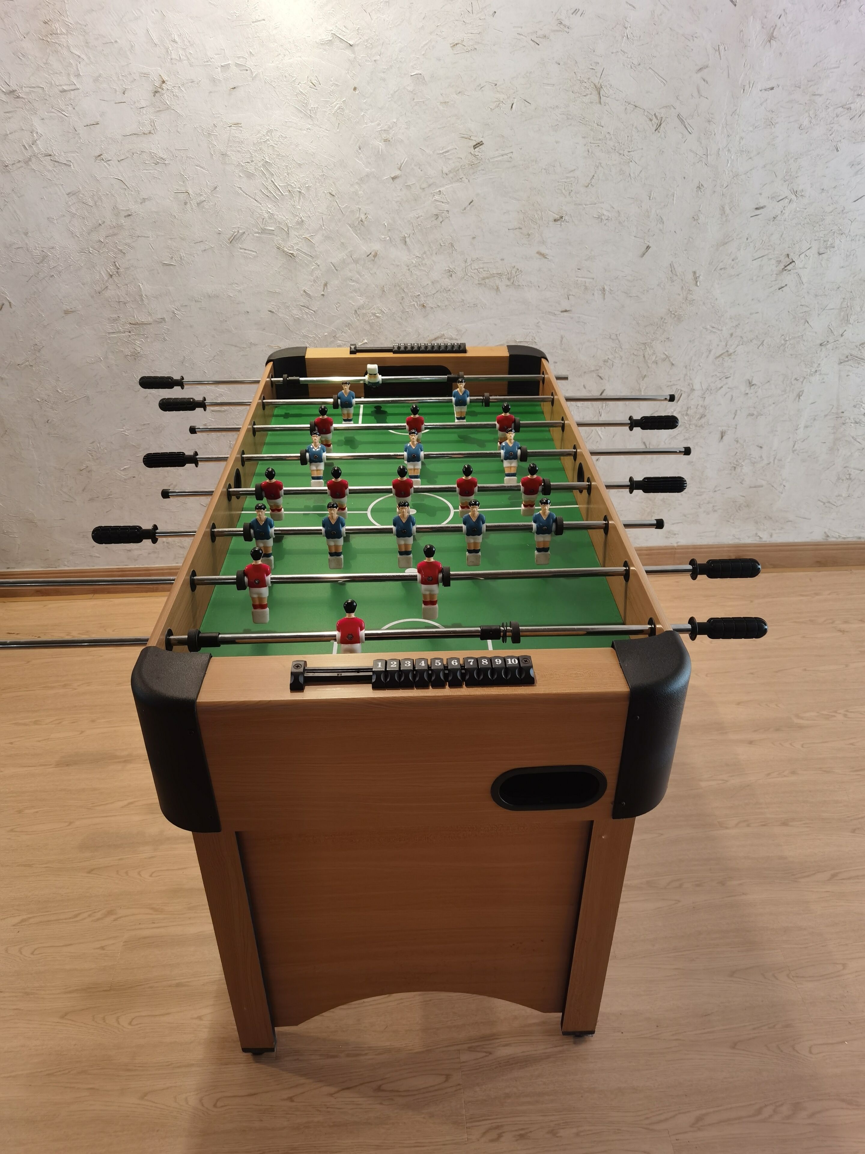 A wooden foosball table with a green playing surface and numbered rods.