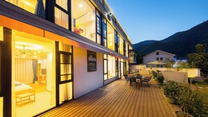 Un hotel con terraza de madera, mobiliario exterior y vistas a las montañas.