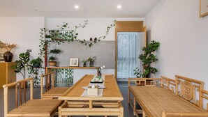 Un comedor con una larga mesa de madera y sillas, rodeado de plantas en macetas y un muro decorativo.