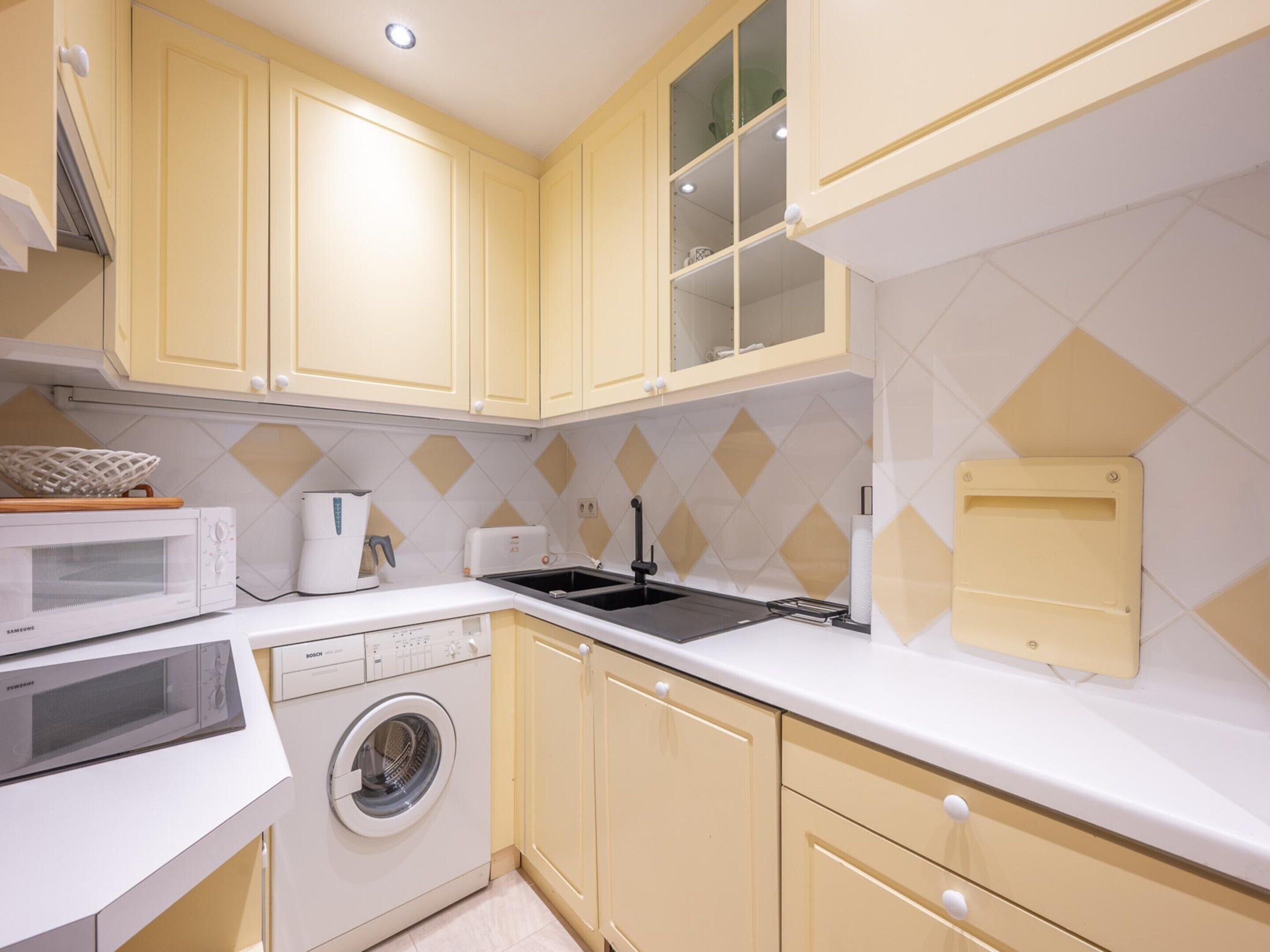 A compact kitchen with yellow cabinets, a microwave, a toaster, a sink, and a washing machine.