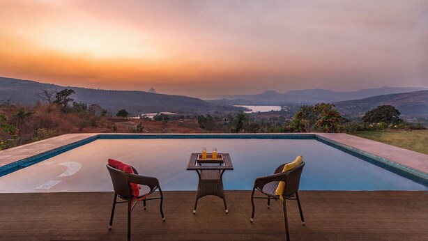 Une piscine avec vue sur les montagnes et sur le coucher de soleil. On y trouve trois chaises et une table avec deux bougies.