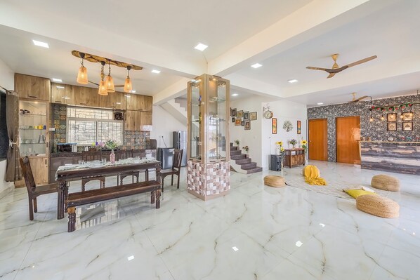 A spacious living area with a marble floor, a dining table set with chairs, a glass cabinet, and a staircase leading to another level.