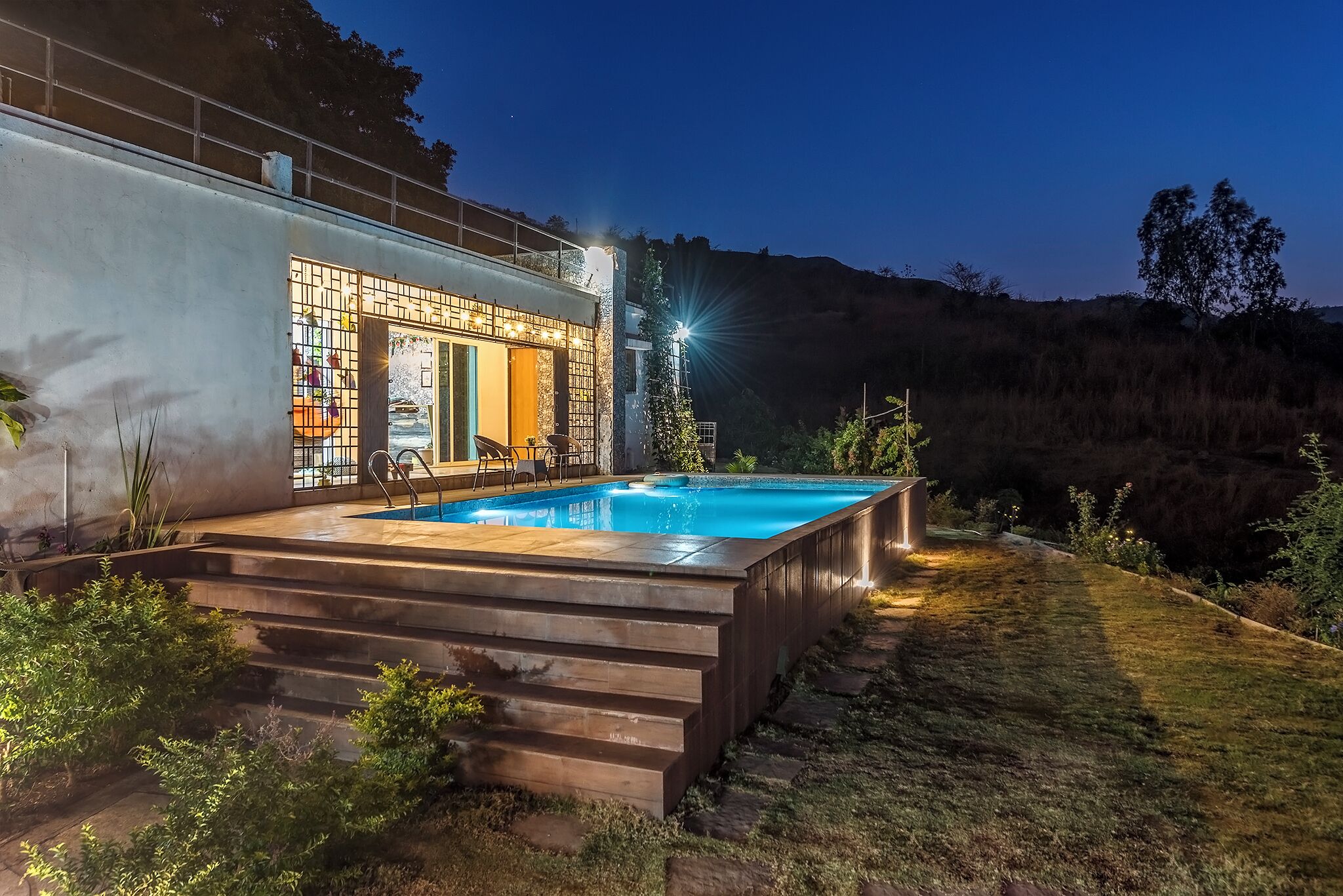 Una casa moderna con piscina, escalones que bajan a la piscina y un exterior bien iluminado.
