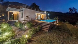 Une maison moderne avec une piscine, entourée d’un jardin bien éclairé et accessible par des marches menant à l’entrée.
