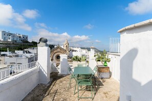Una terraza en la azotea con una mesa y sillas, una planta de cactus y vistas a edificios e iglesia al fondo.
