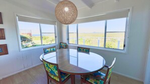 Comedor con mesa redonda y sillas, ventanas amplias con vistas, y una lámpara colgante.
