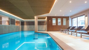 Ein modernes Hallenbad mit klarem Wasser, Liegestühlen und einer Holzdeckenkonstruktion.