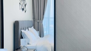 A modern hotel room with a grey upholstered headboard, white bedding, and a bedside table with a lamp. - Luxurious Belvilla 1BR JVC with Pool, Gym & BBQ Access (Dubai)