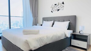 A modern hotel room with a large bed, a nightstand, and a city view. - Luxurious Belvilla 1BR JVC with Pool, Gym & BBQ Access (Dubai)