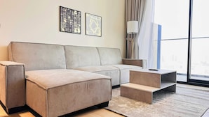 A modern living room with a sectional sofa, a coffee table, and a small side table. There are two framed artworks on the wall and a floor lamp. - Luxurious Belvilla 1BR JVC with Pool, Gym & BBQ Access (Dubai)
