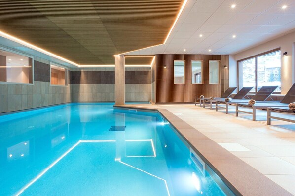 Una piscina interior moderna con agua cristalina, sillones de descanso y un diseño de techo de madera.