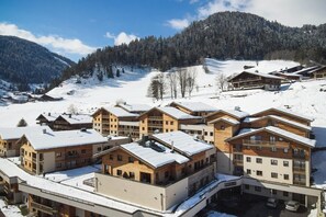 A snow-covered resort with multiple wooden buildings, including a central building with a balcony and a smaller building with a ski lift.