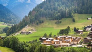 A mountain lodge with multiple buildings, surrounded by lush green fields and dense forest.