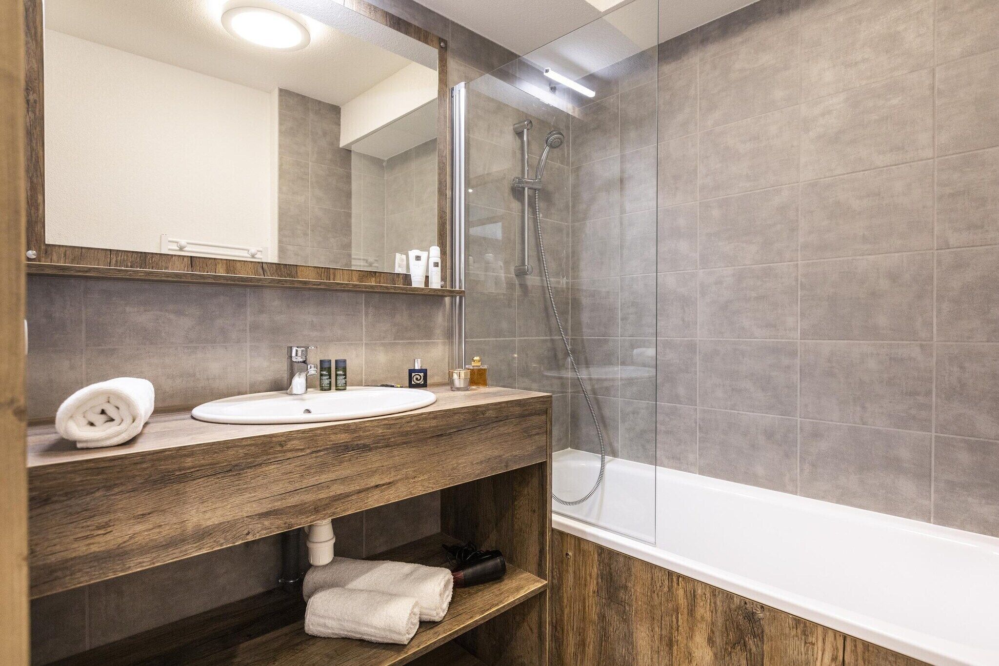 A modern bathroom with a wooden vanity, a white sink, a large mirror, a shower area, and a bathtub.