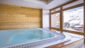 A hot tub in a room with wooden walls and large windows overlooking a snowy mountain. - Apartment in France with Pool and Spa (St Martin de Belleville)