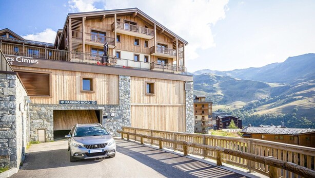 A multi-story wooden building with balconies, a stone facade, and a car parked in front. - Apartment in France with Pool and Spa (St Martin de Belleville)