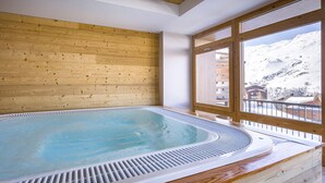Ein Whirlpool in einem Zimmer mit Holzwänden und großen Fenstern mit Blick auf einen verschneiten Berg.