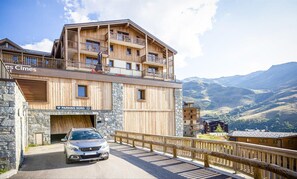 Un edificio de madera de varios pisos, con balcones, fachada de piedra y un coche estacionado adelante.