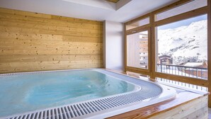 A hot tub in a room with wooden walls and large windows overlooking a snowy mountain.