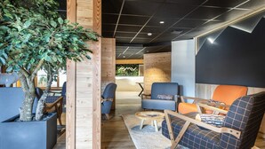 A modern lounge area with wooden accents, seating, and a large tree. - Apartment in Risoul with Ski-In/Ski-Out Access (RISOUL)