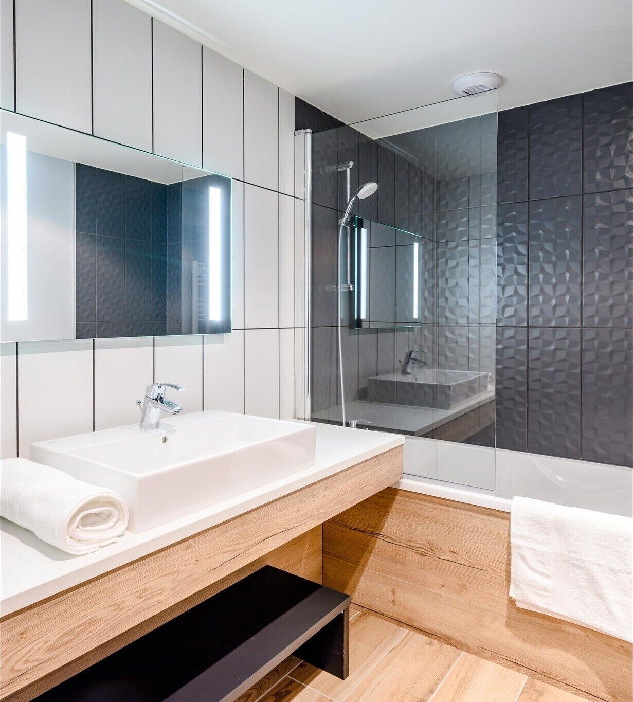 Une salle de bain moderne avec un lavabo blanc, un miroir et une douche séparée par une paroi de verre.