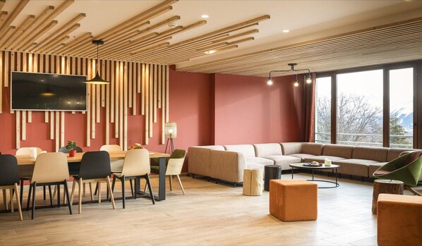 A modern living room with a large TV, wooden slats on the ceiling, a sofa, and a dining area with chairs and a table.