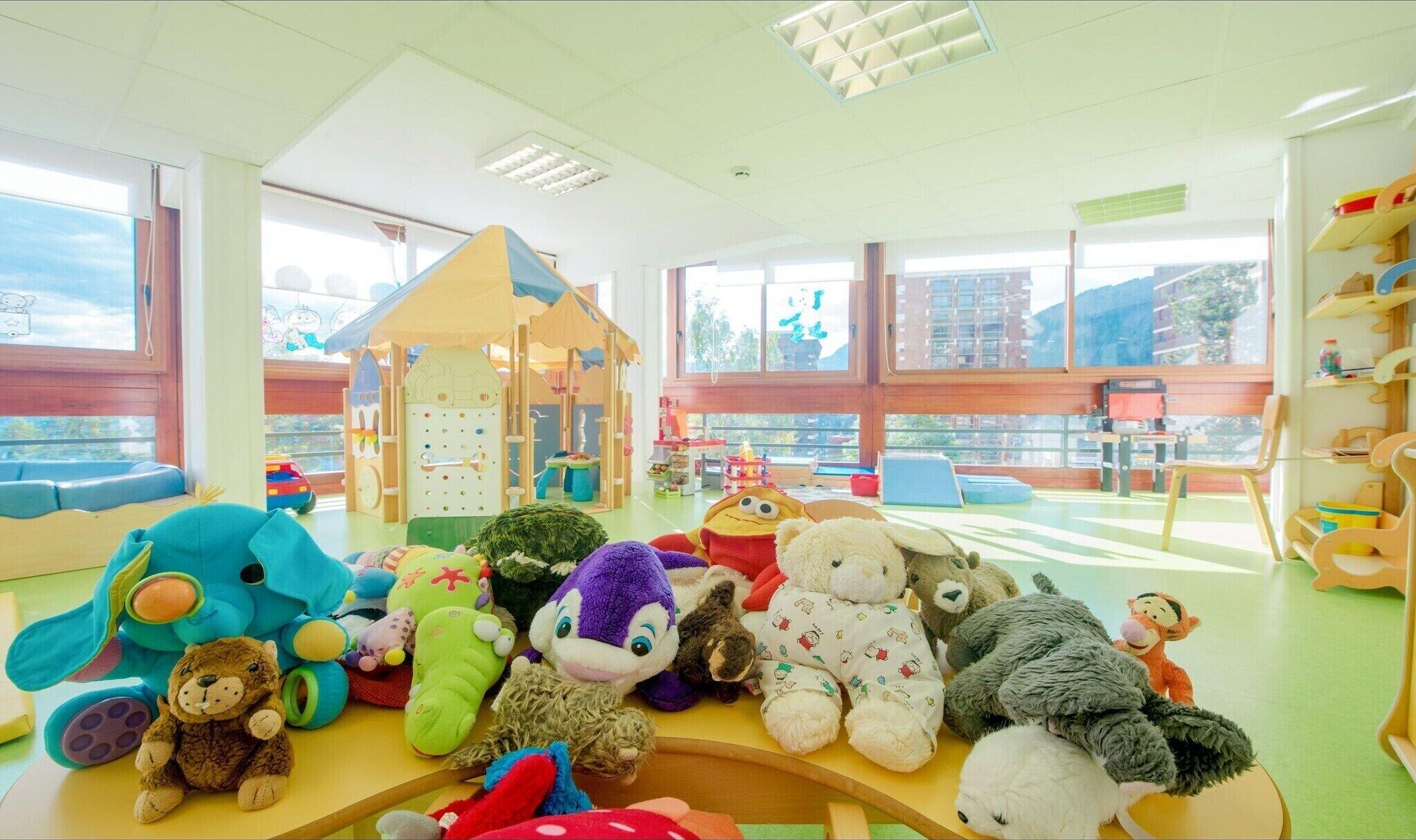 Une salle de jeux lumineuse, dotée de grandes fenêtres, d’une maisonnette et de divers jouets pour enfants.