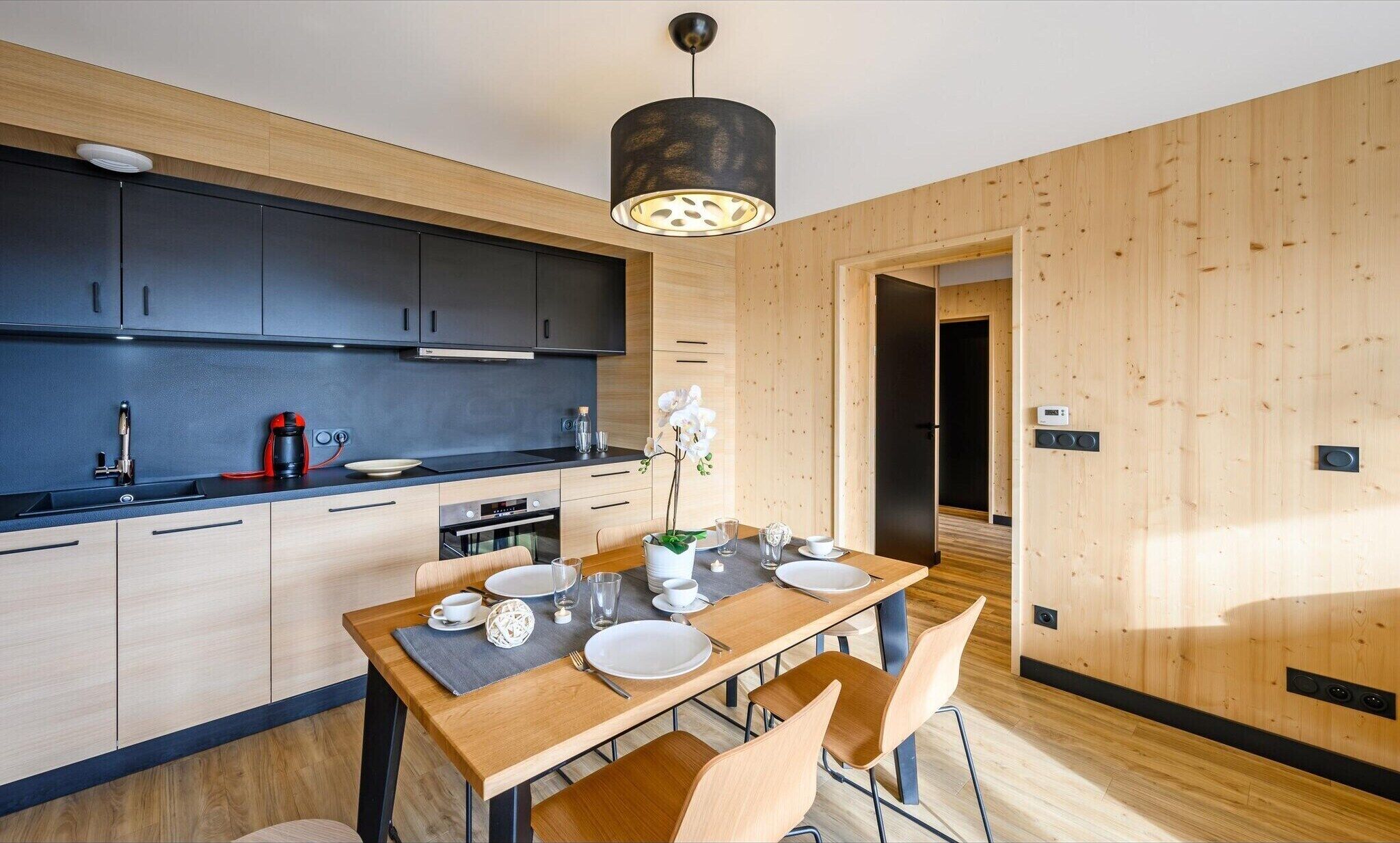 A modern kitchen with dark cabinets, a wooden dining table set for four, and a pendant light above.