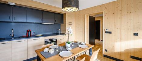 A modern kitchen with dark cabinets, a wooden dining table set for four, and a pendant light above.