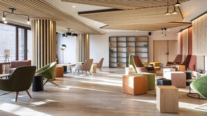Un espace de détente moderne avec un plancher en bois, de nombreux sièges, notamment des fauteuils et des poufs, et une grande bibliothèque.