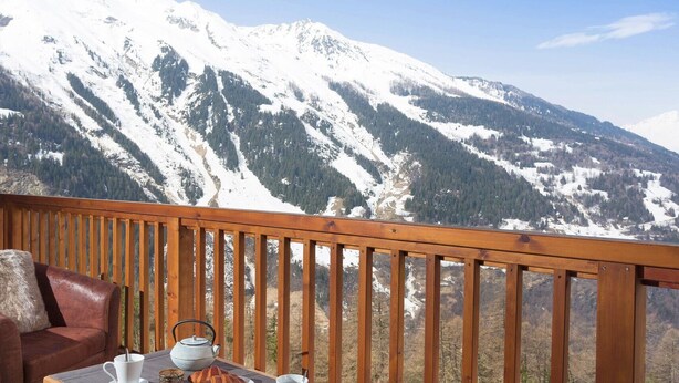 A balcony with a wooden railing, a leather chair, a table with a teapot, and a cup. - Apartment in Sainte-Foy with Ski-In/Ski-Out (Sainte-Foy Tarentaise)