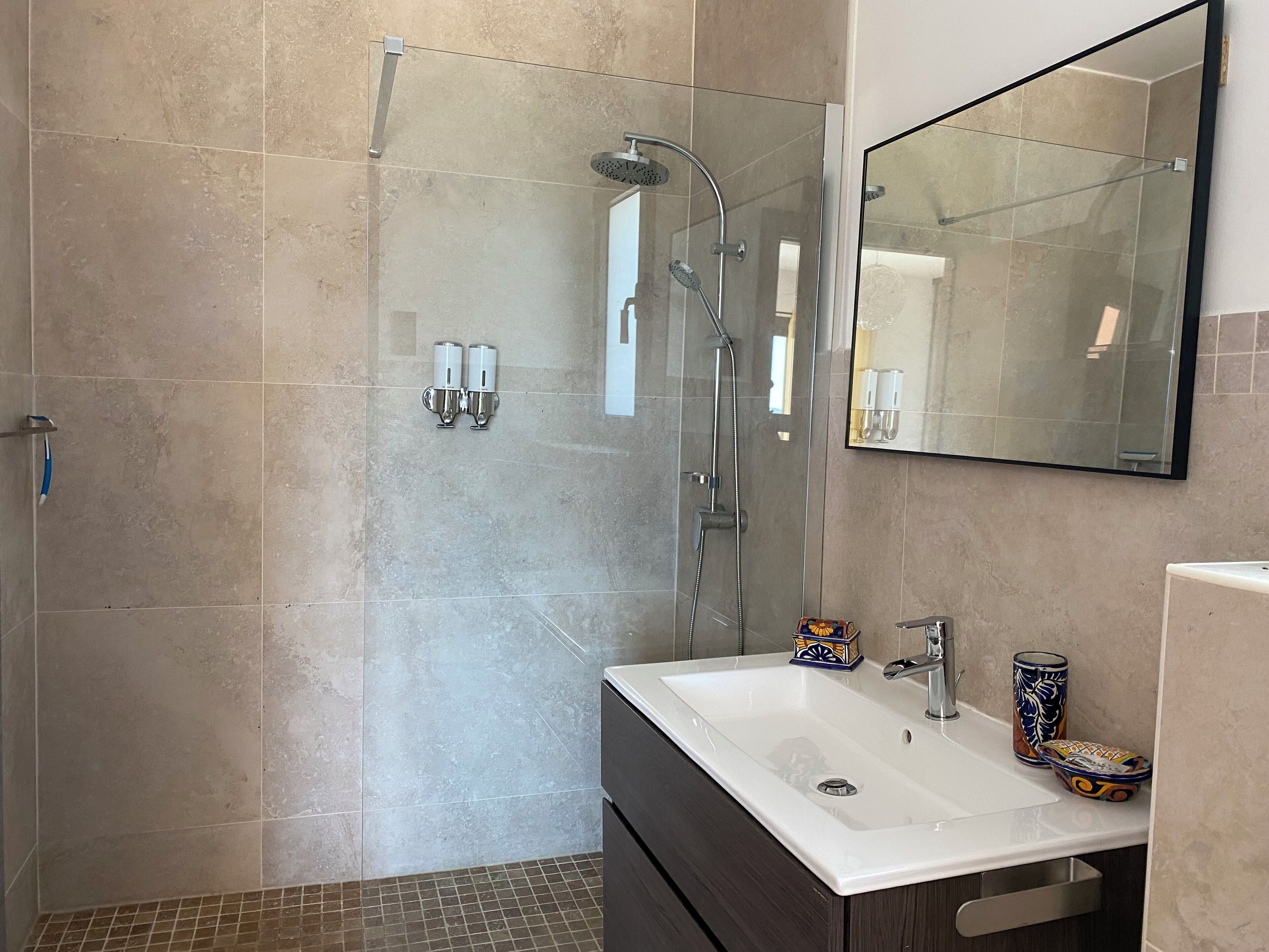 A modern bathroom with a glass-enclosed shower, a white sink, and a large mirror.