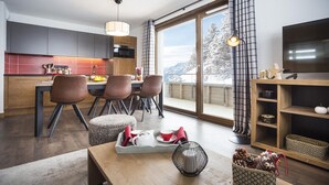 Een moderne keuken met een eethoek, grote ramen met uitzicht op met sneeuw bedekte bomen en een televisie op een houten plank.