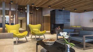 Een moderne zithoek met gele fauteuils, een blauwe bank en een open haard.