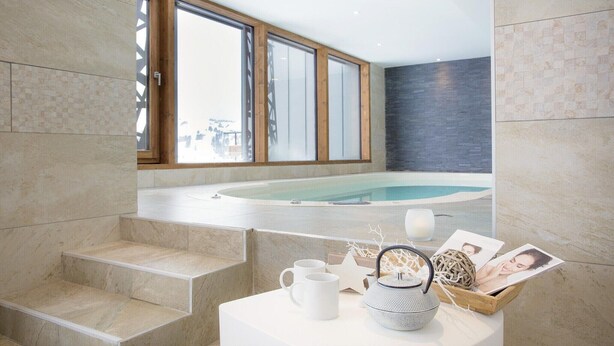 Een moderne badkamer met een groot bad, een klein tafeltje met decoratieve objecten en een uitzicht op een besneeerd landschap door grote ramen.