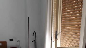 Une chambre d’hôtel avec un lit, une table de chevet avec une lampe, un plancher en bois et une vue par une fenêtre équipée de stores.