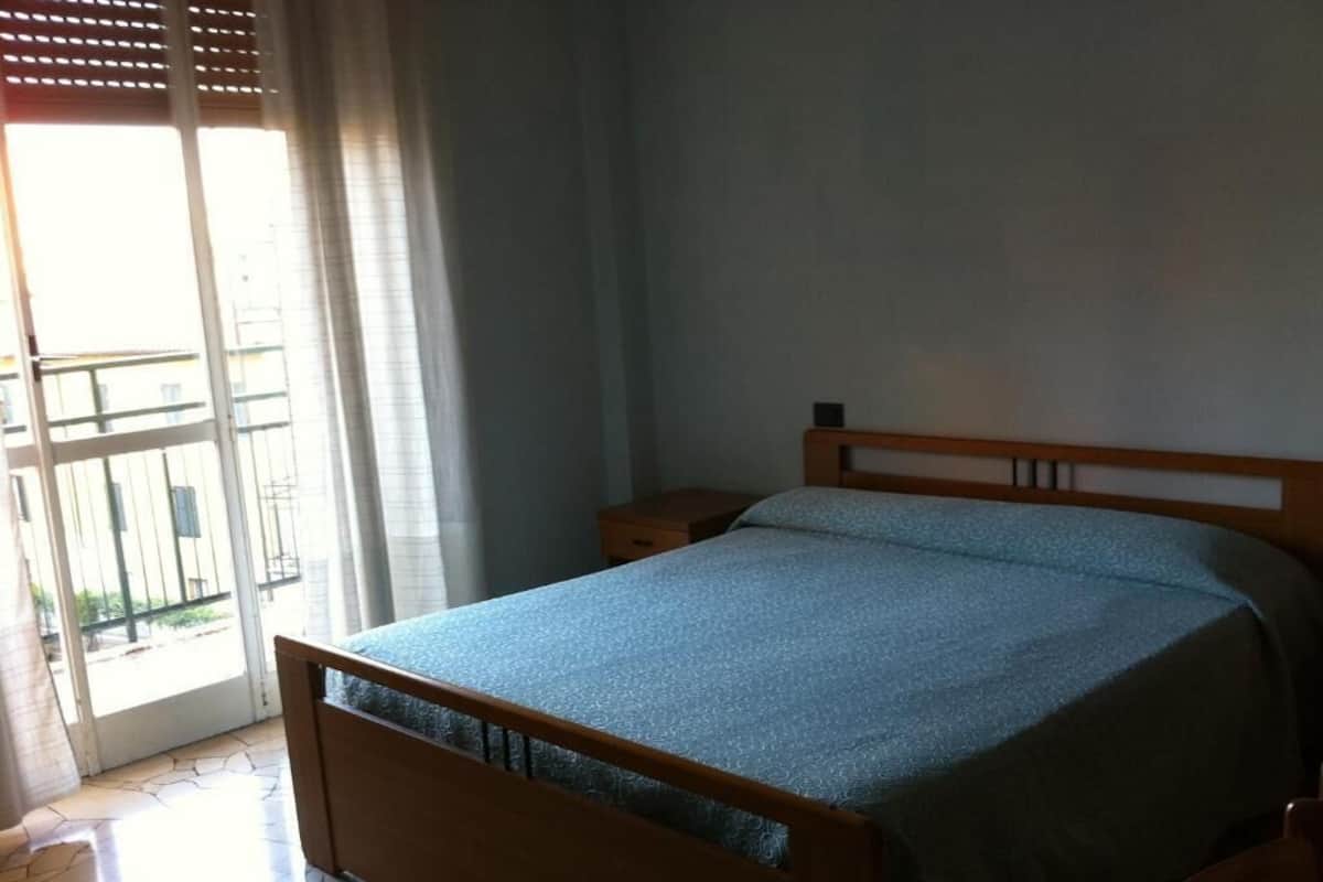 Quarto com cama de madeira, mesa de cabeceira e janela com persianas.