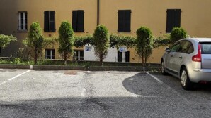 A parking lot with a car, a building with multiple windows and shutters, and a few trees. - Hotel Mira (Varese)
