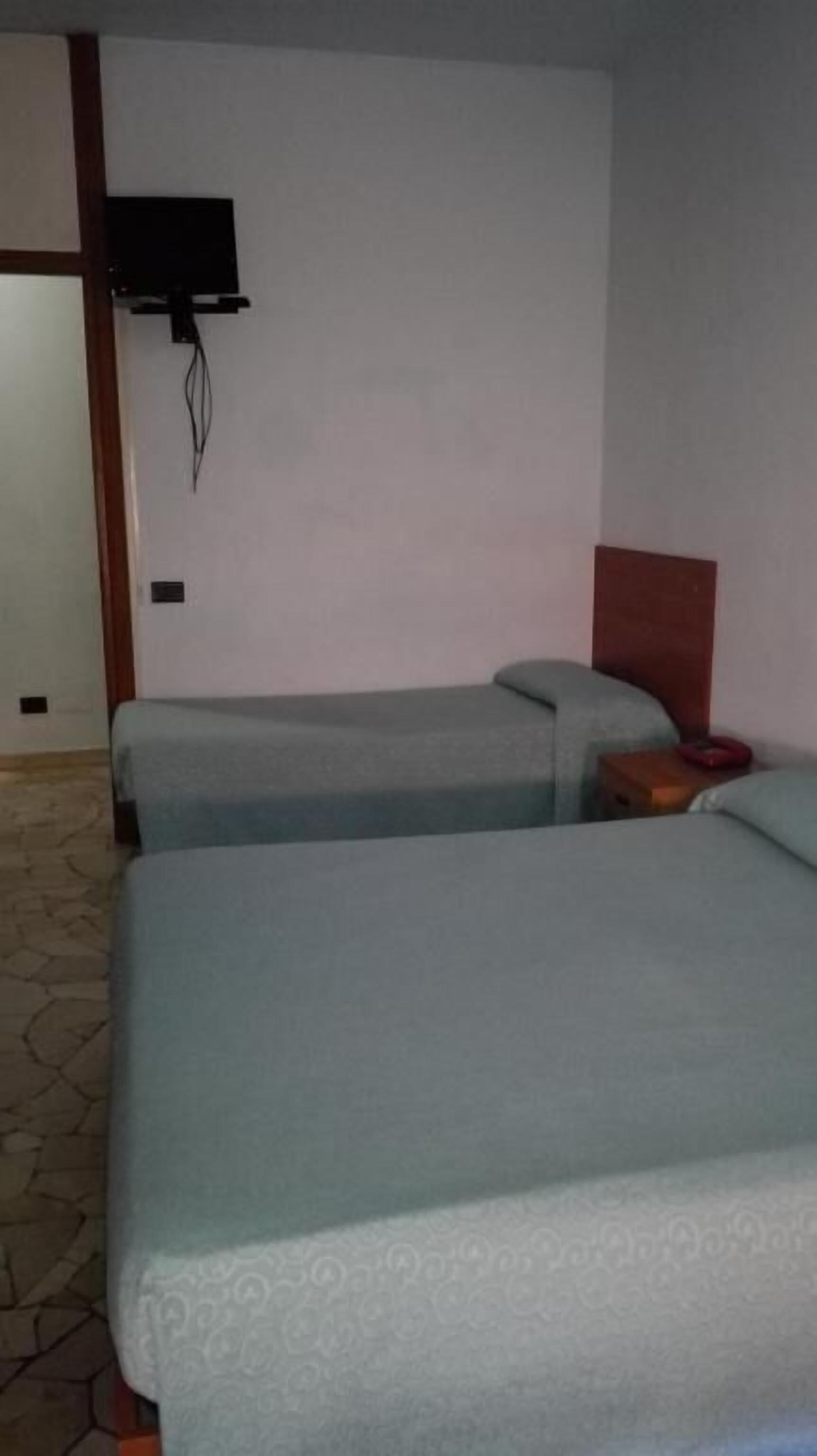 Habitación de hotel con dos camas, cabecero de madera, televisor montado en la pared y piso estampado.