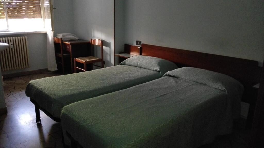 A room with two single beds, a wooden desk, a chair, and a radiator.