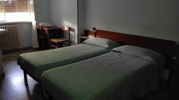 A room with two single beds, a wooden desk, a chair, and a radiator.