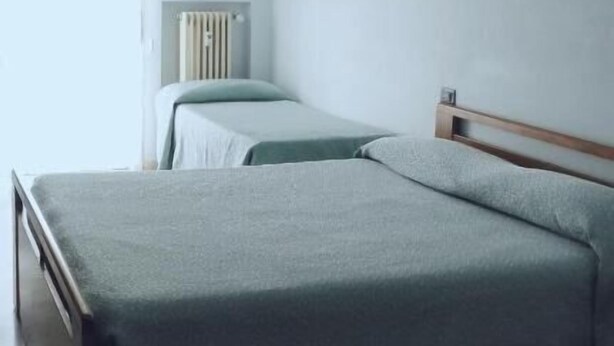A bedroom with two beds, a radiator, and a window with curtains. - Hotel Mira (Varese)
