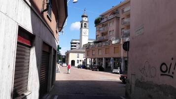 A street view with a clock tower, buildings with balconies, and a pedestrian.