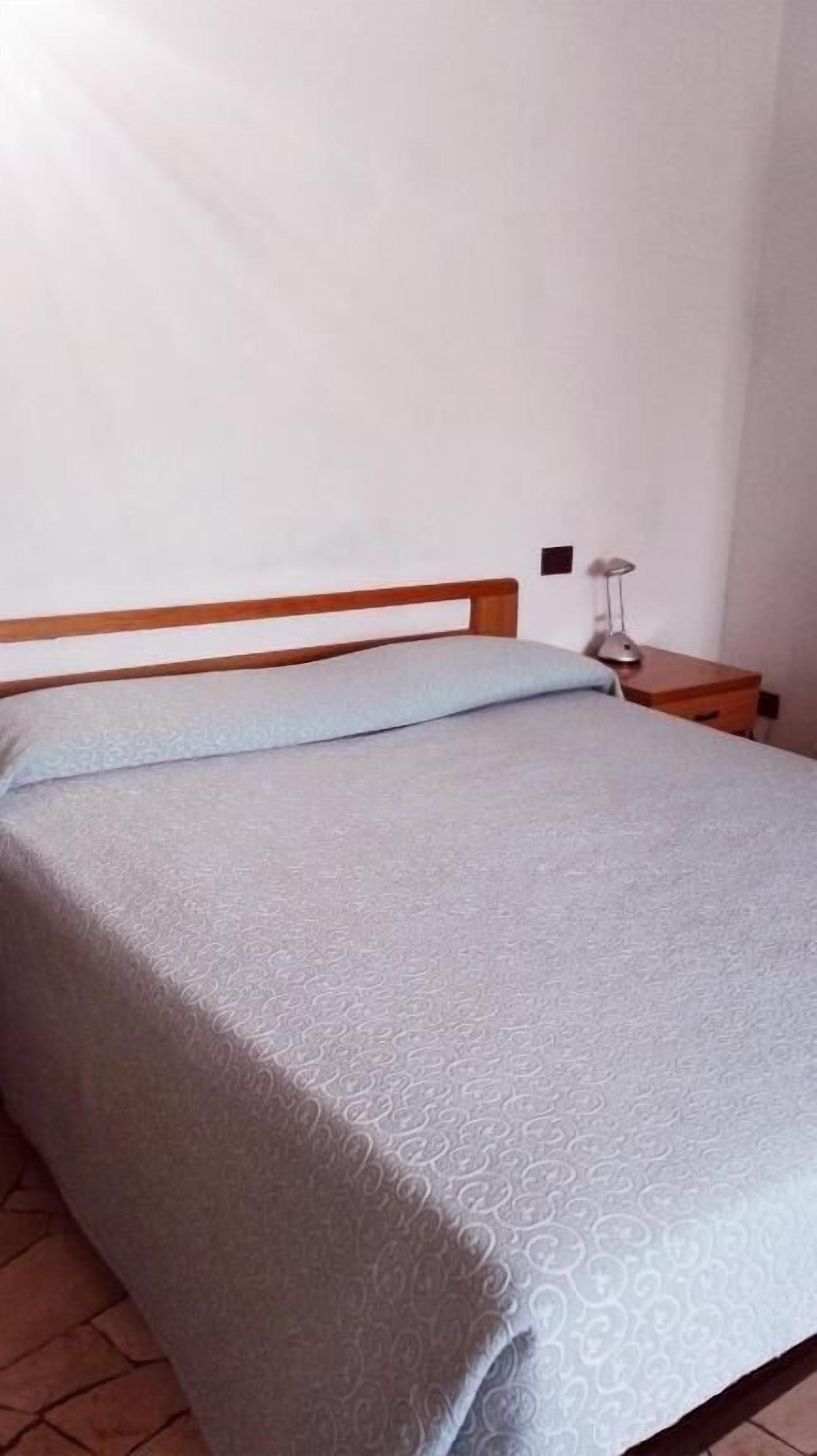 Ein Bett mit hölzernem Kopfteil, einer grau gemusterten Tagesdecke und einem Nachttisch mit Lampe.