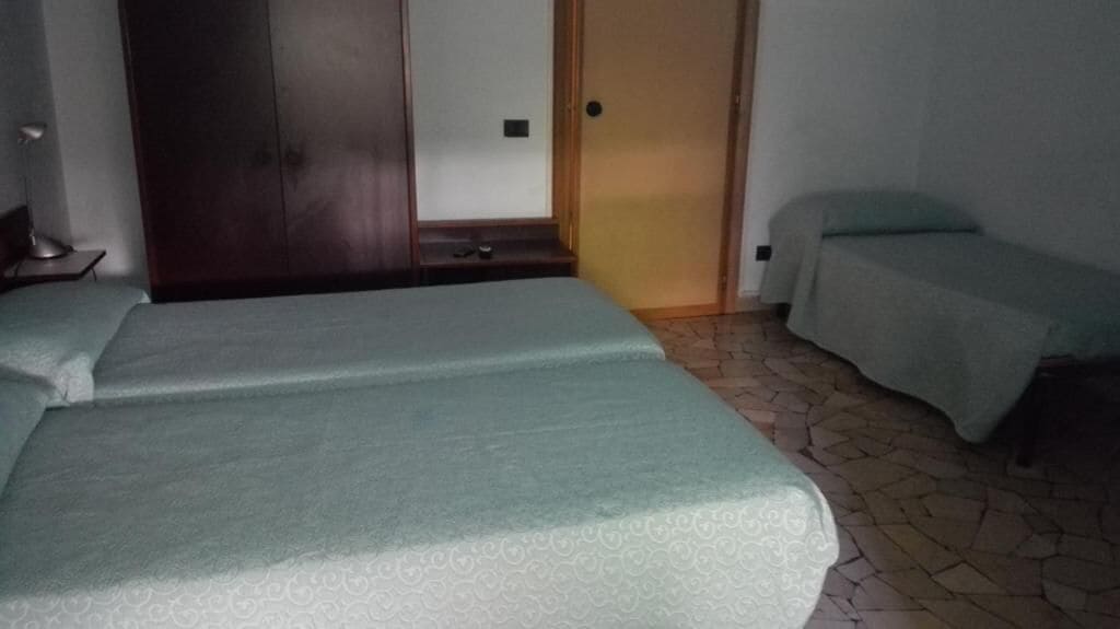 A room with two beds, a wardrobe, and a door leading to another room.