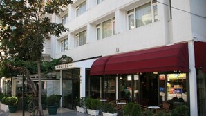 Un hôtel avec un auvent rouge, des tables à l’extérieur et des plantes en pot.